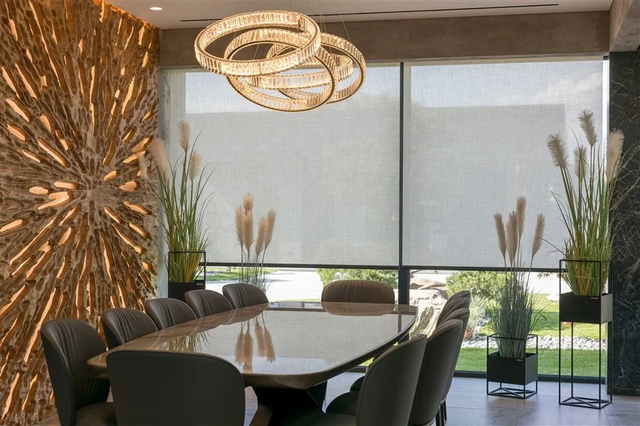 Roller shades lowered across a dining room window wall