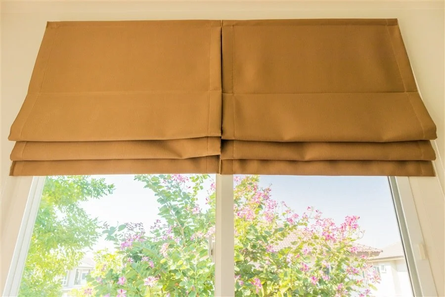 Tan Roman shades with folded fabric panels above a window